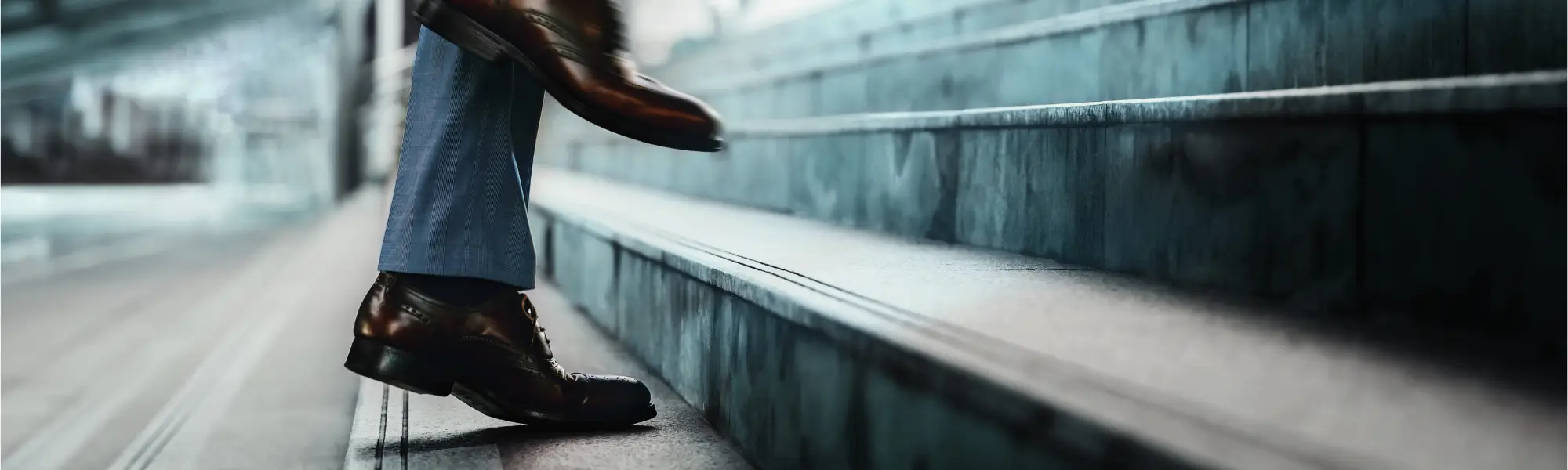 A person in a dark suit and smart shoes ascending stairs.